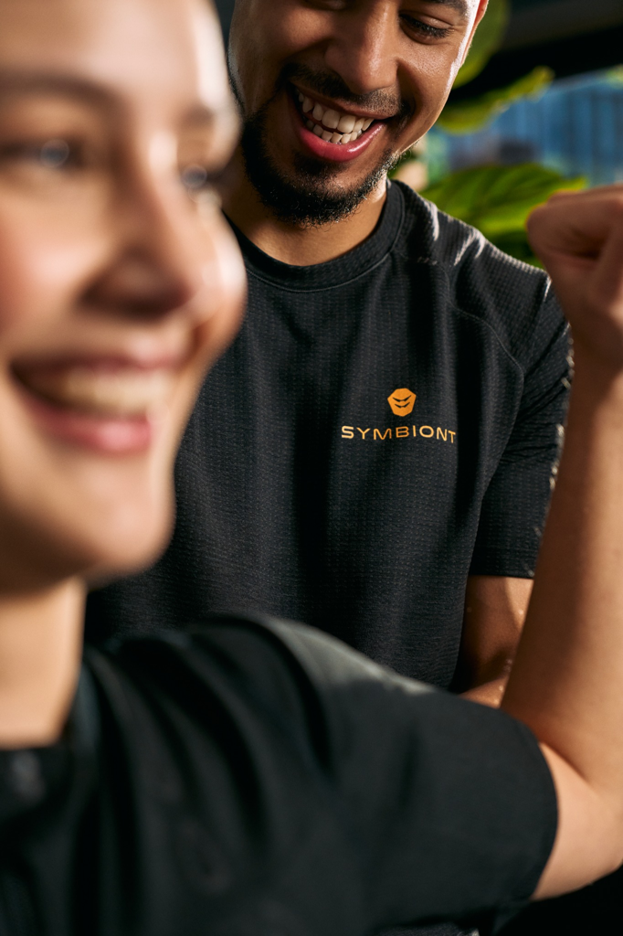 Grande plano de um cliente e de um personal trainer a discutir sobre fitness e objetivos de treino num estúdio TechBody para a melhor experiência de treino com SYMBIONT.